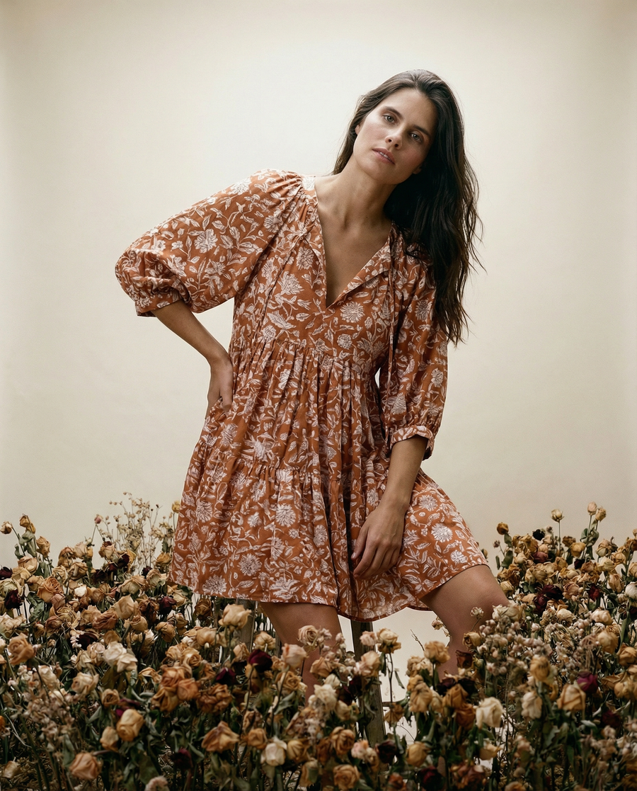 Woman in a floral dress standing among dried flowers against a neutral background