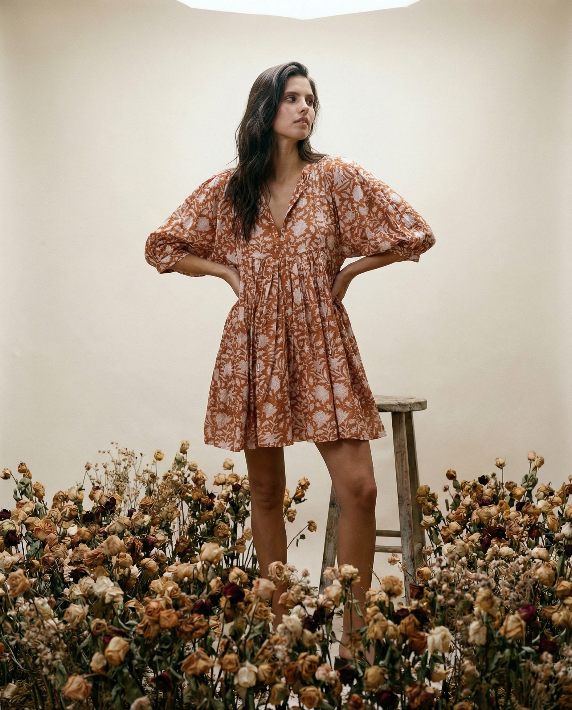 Woman in a floral dress standing in a field of flowers with a neutral background